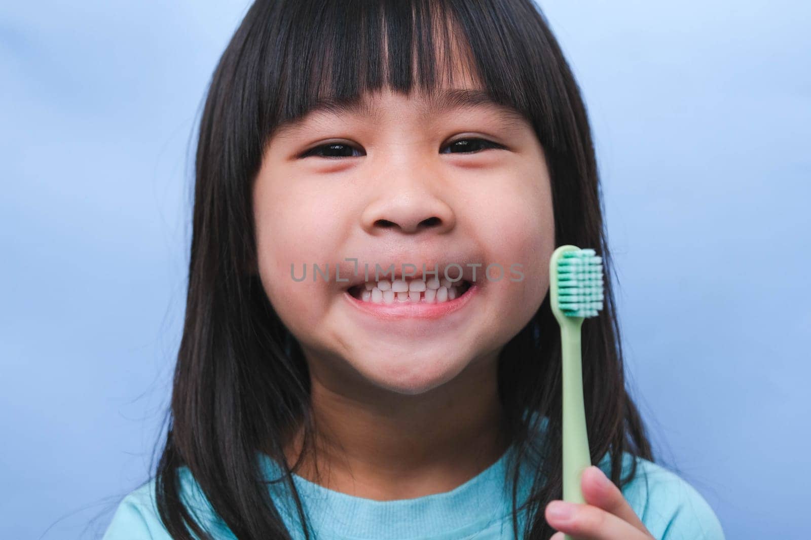 Smiling cute little girl holding toothbrush isolated on blue background. Cute little child brushing teeth. Kid training oral hygiene, Tooth decay prevention or dental care concept. by TEERASAK