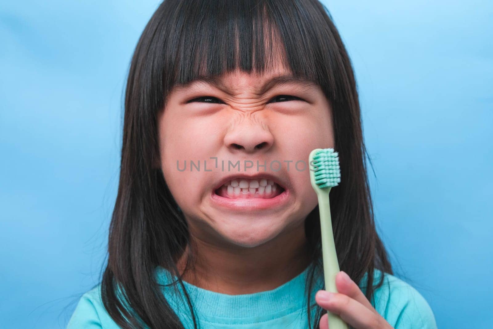 Smiling cute little girl holding toothbrush isolated on blue background. Cute little child brushing teeth. Kid training oral hygiene, Tooth decay prevention or dental care concept. by TEERASAK