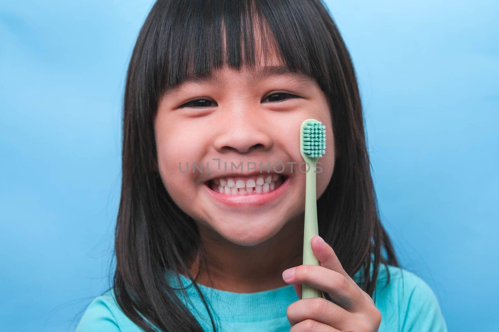 Smiling cute little girl holding toothbrush isolated on blue background. Cute little child brushing teeth. Kid training oral hygiene, Tooth decay prevention or dental care concept. by TEERASAK