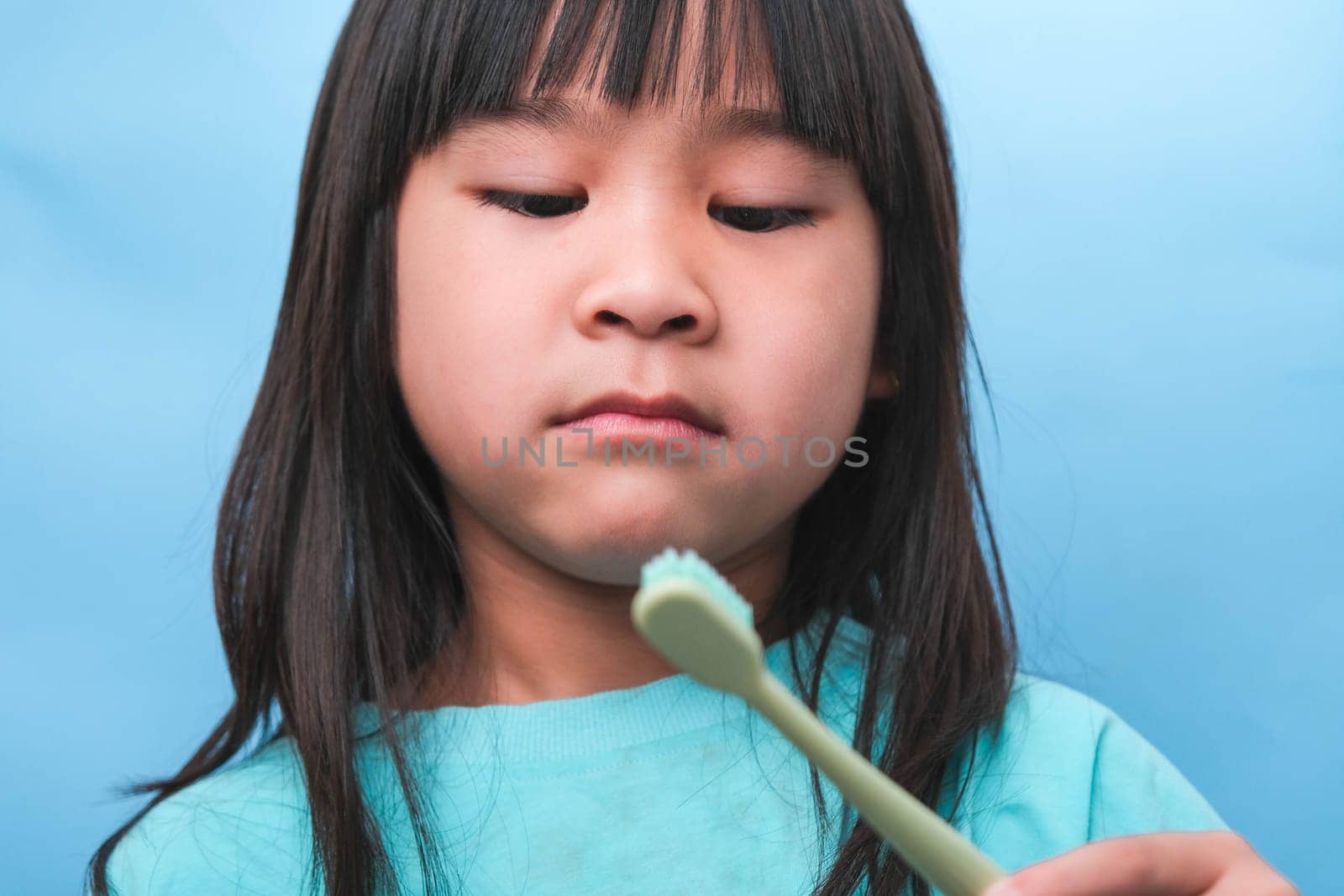 Smiling cute little girl holding toothbrush isolated on blue background. Cute little child brushing teeth. Kid training oral hygiene, Tooth decay prevention or dental care concept. by TEERASAK