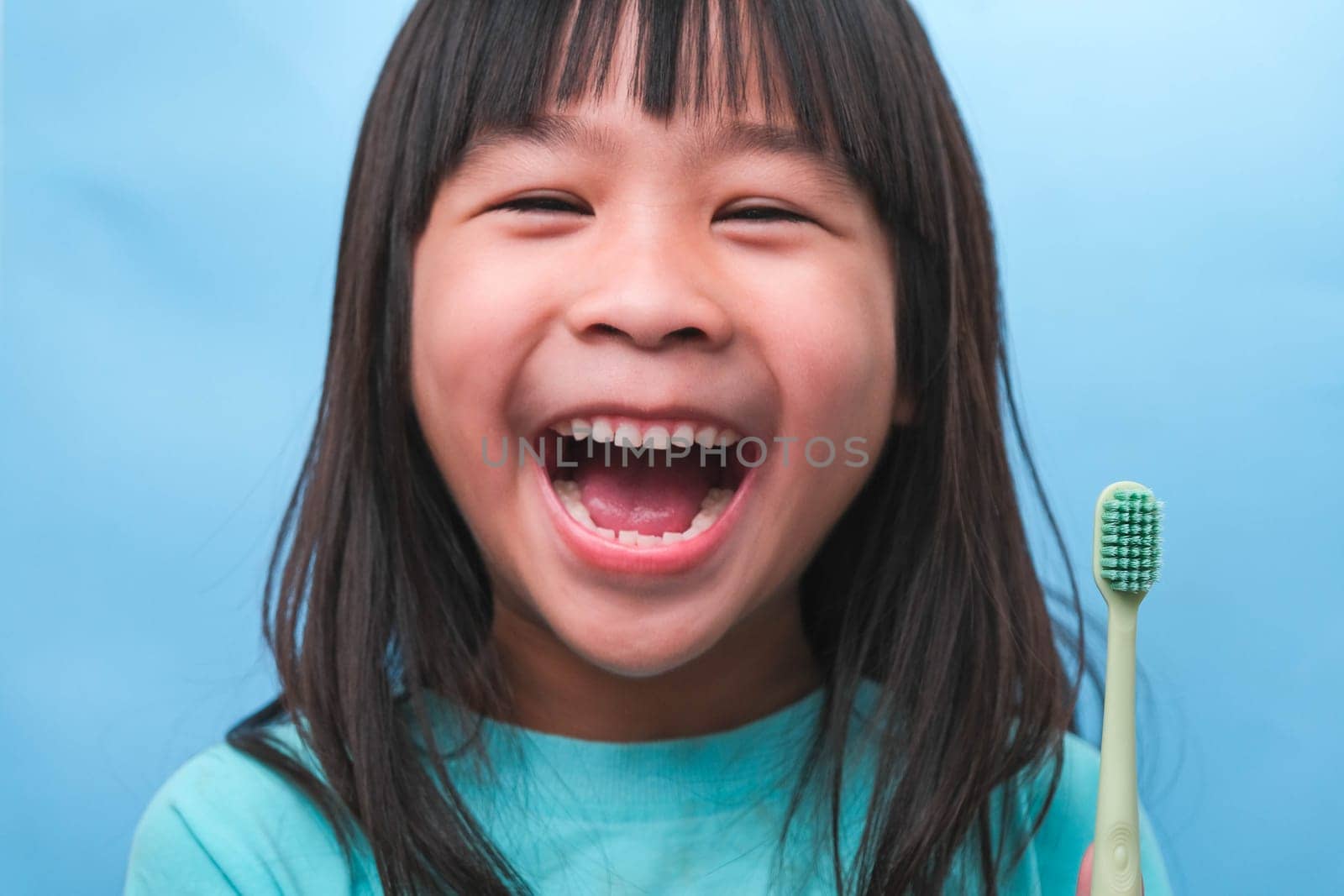 Smiling cute little girl holding toothbrush isolated on blue background. Cute little child brushing teeth. Kid training oral hygiene, Tooth decay prevention or dental care concept.