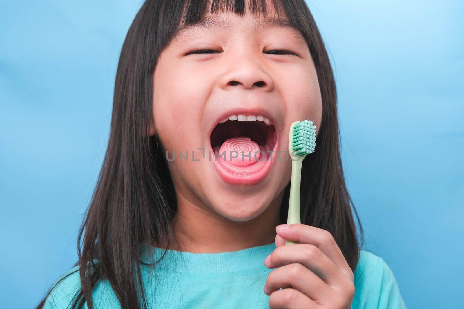 Smiling cute little girl holding toothbrush isolated on blue background. Cute little child brushing teeth. Kid training oral hygiene, Tooth decay prevention or dental care concept.