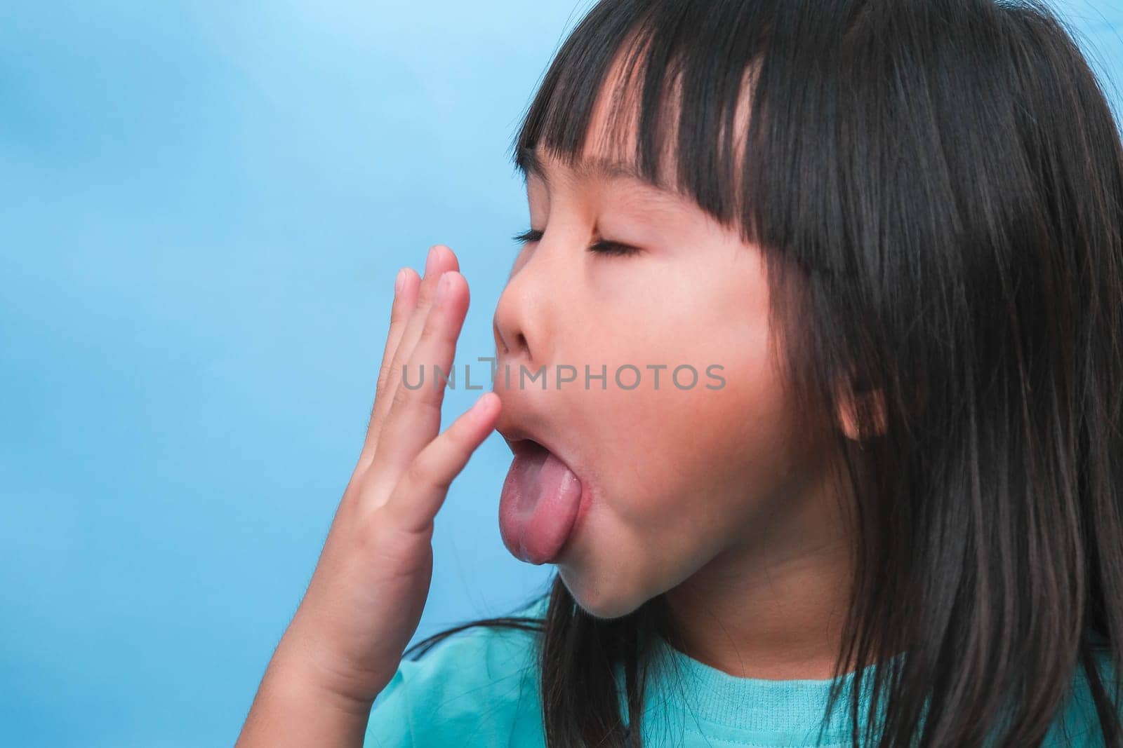 Little asian girl covering her mouth to smell the bad breath. Child girl checking breath with her hands. Oral health problems or dental care concept. by TEERASAK