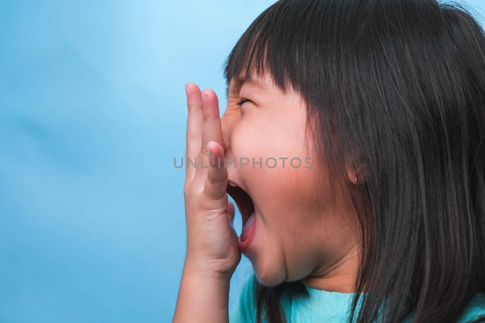 Little asian girl covering her mouth to smell the bad breath. Child girl checking breath with her hands. Oral health problems or dental care concept.