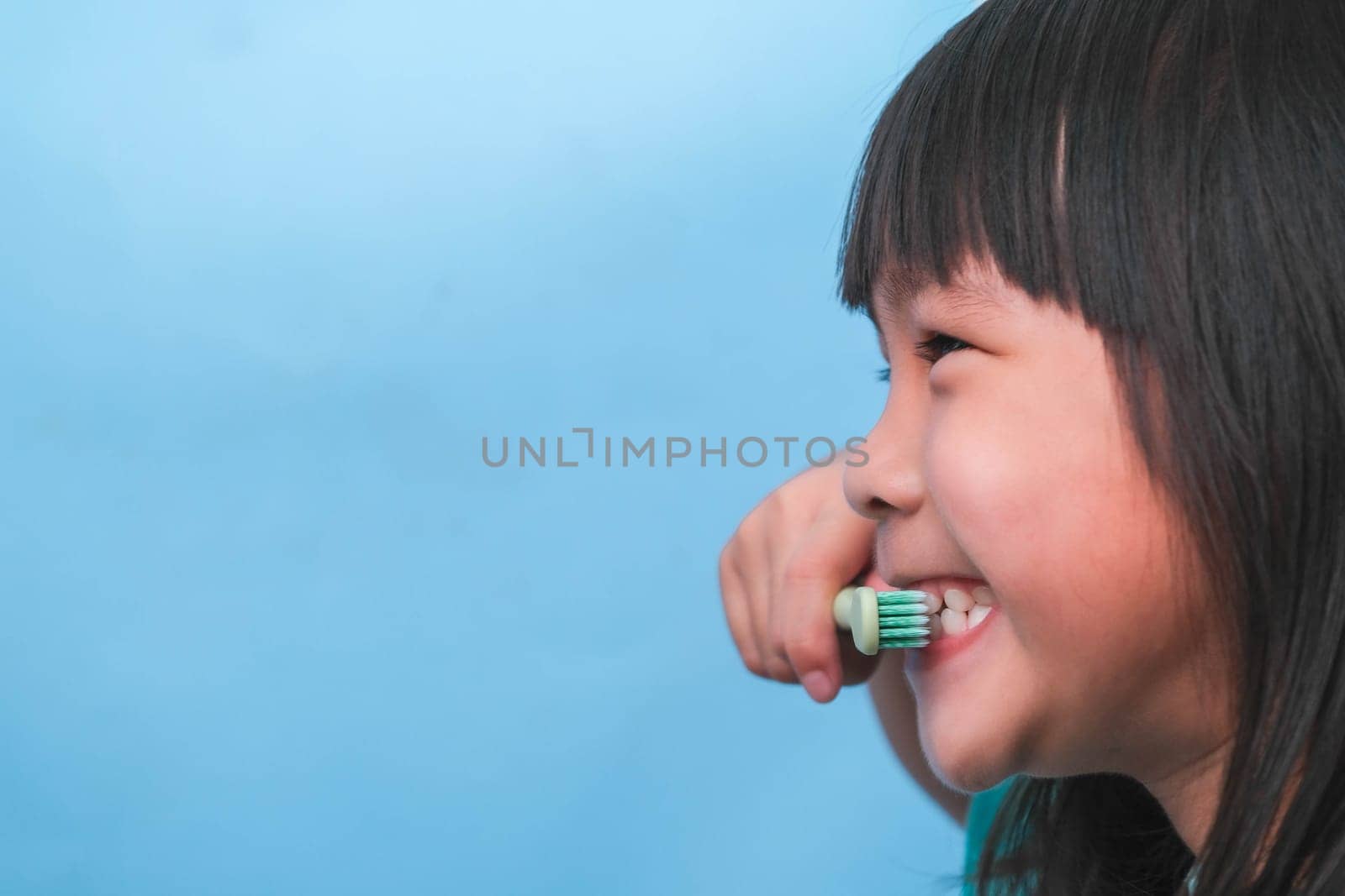 Smiling cute little girl holding toothbrush isolated on blue background. Cute little child brushing teeth. Kid training oral hygiene, Tooth decay prevention or dental care concept. by TEERASAK