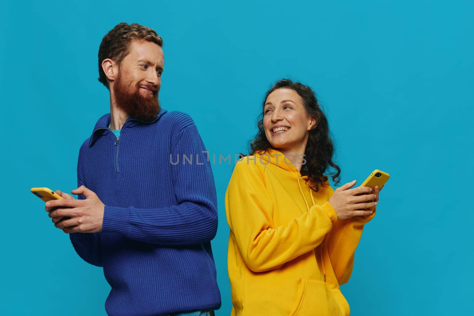 Woman and man cheerful couple with phones in their hands crooked smile cheerful, on blue background. The concept of real family relationships, talking on the phone, work online. High quality photo