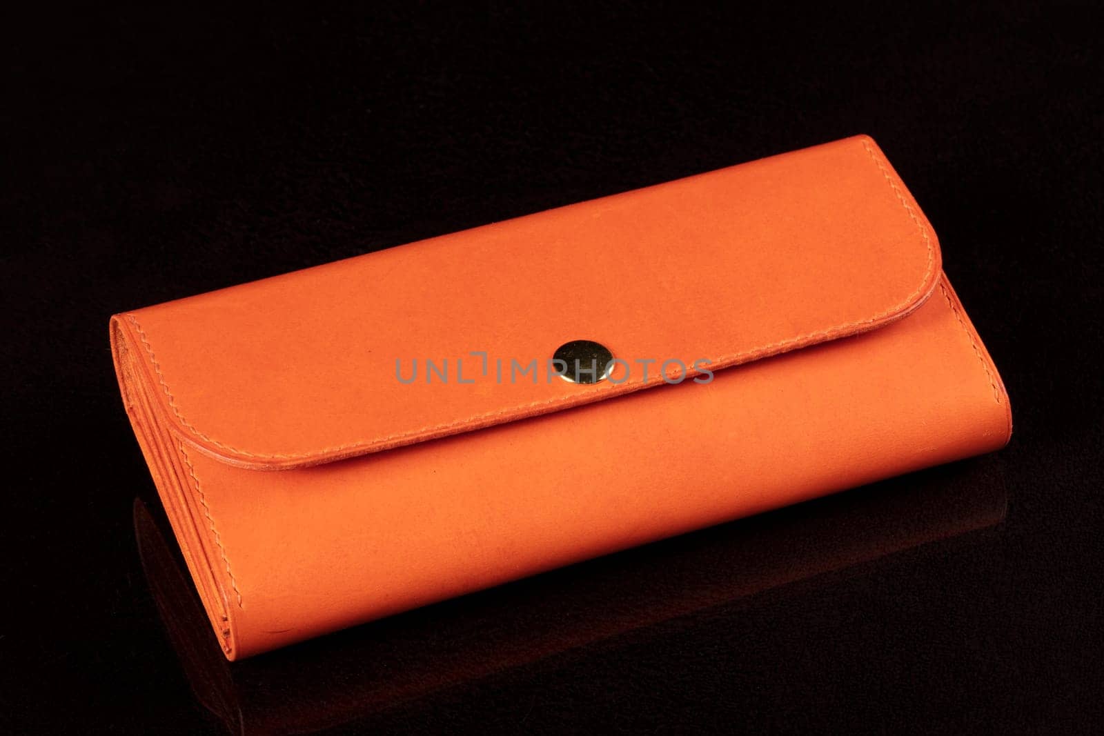Orange leather wallet on a dark background. by Sviatlana