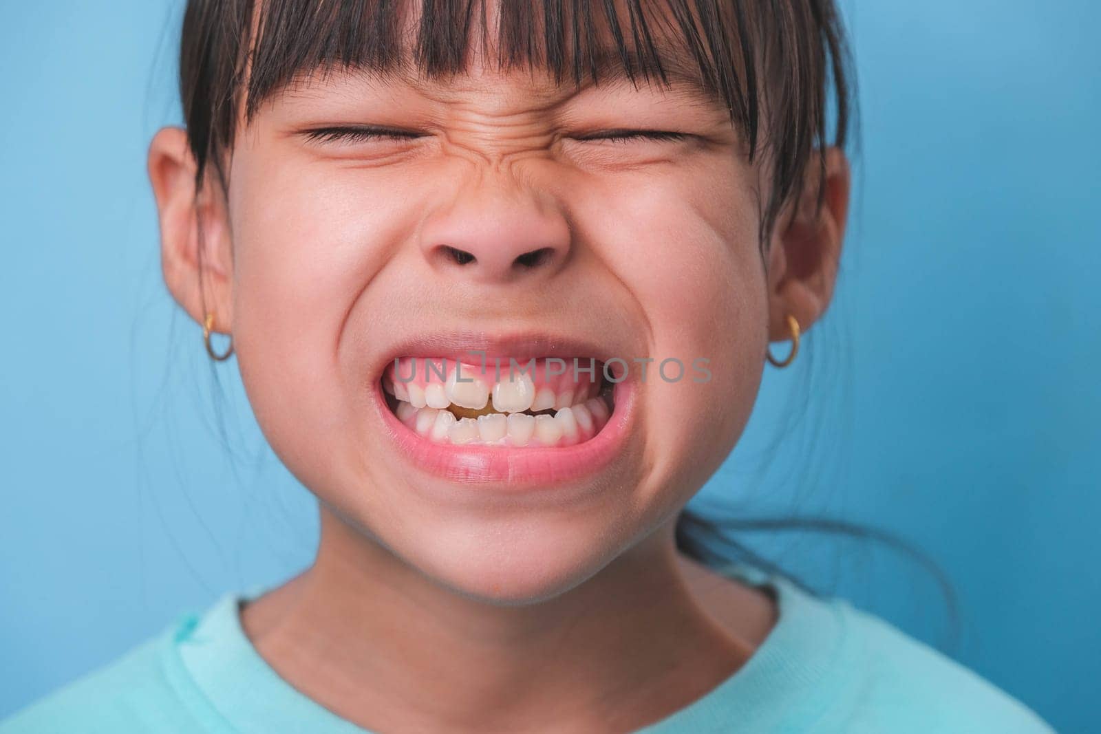Close-up of smiling young girl revealing her beautiful white teeth on a blue background. Concept of good health in childhood. by TEERASAK