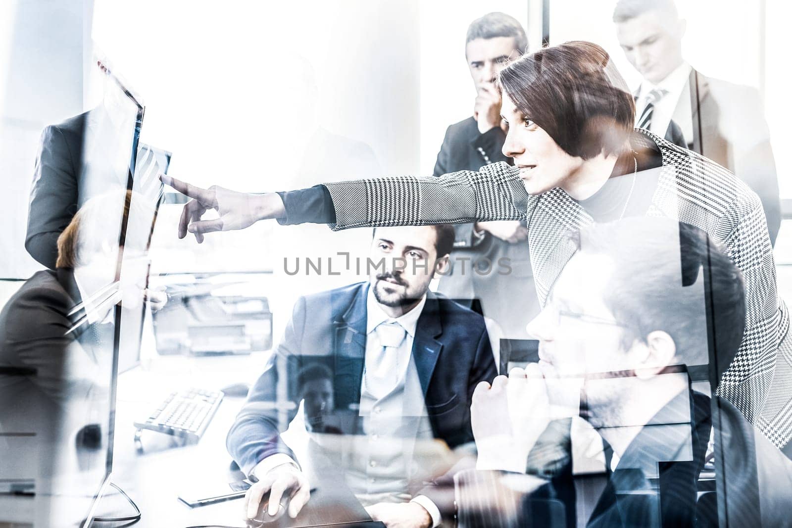 Business team looking at data on multiple computer screens in corporate office. Businesswoman pointing on screen. Business people trading online. Business, entrepreneurship and team work concept.