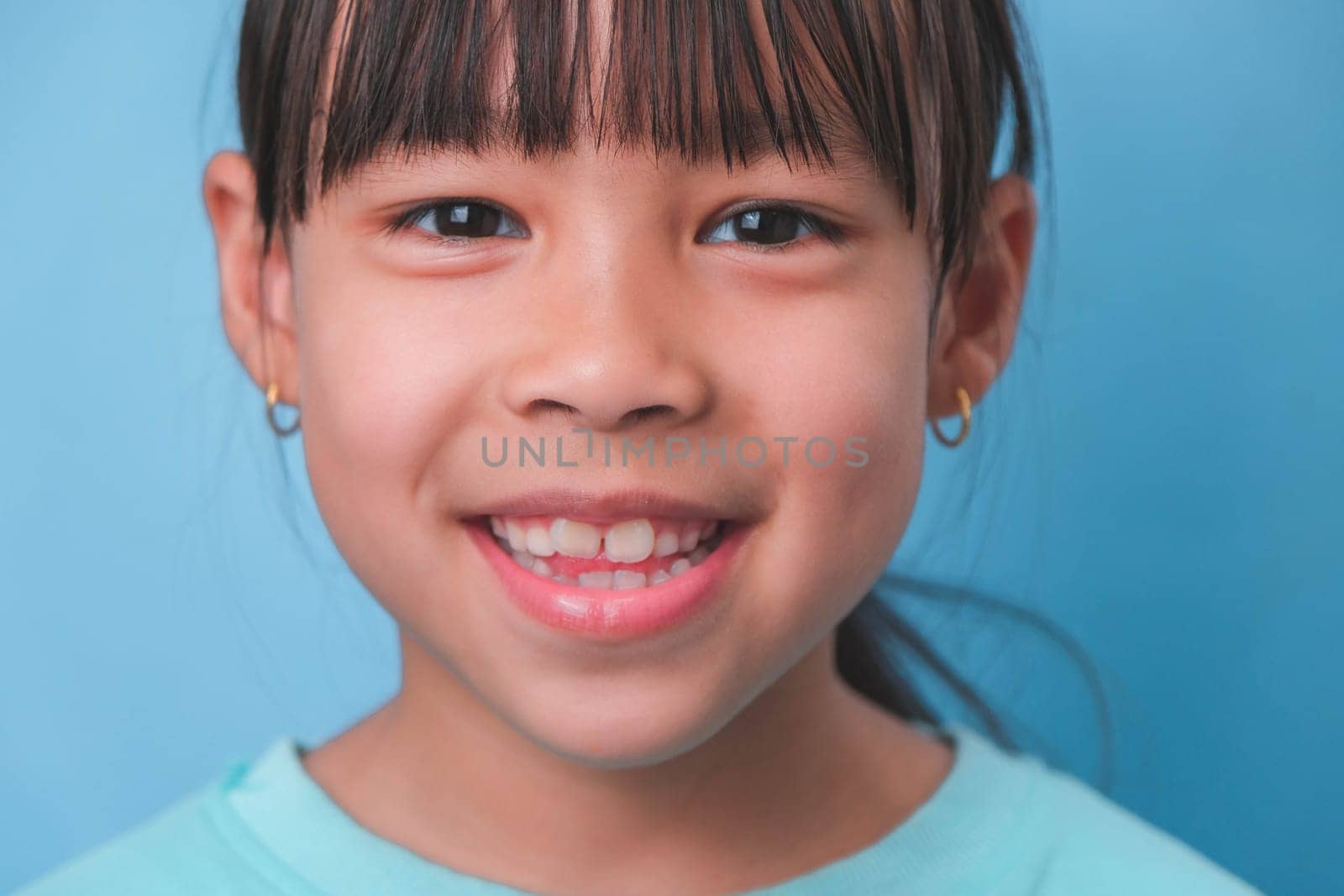 Close-up of smiling young girl revealing her beautiful white teeth on a blue background. Concept of good health in childhood.