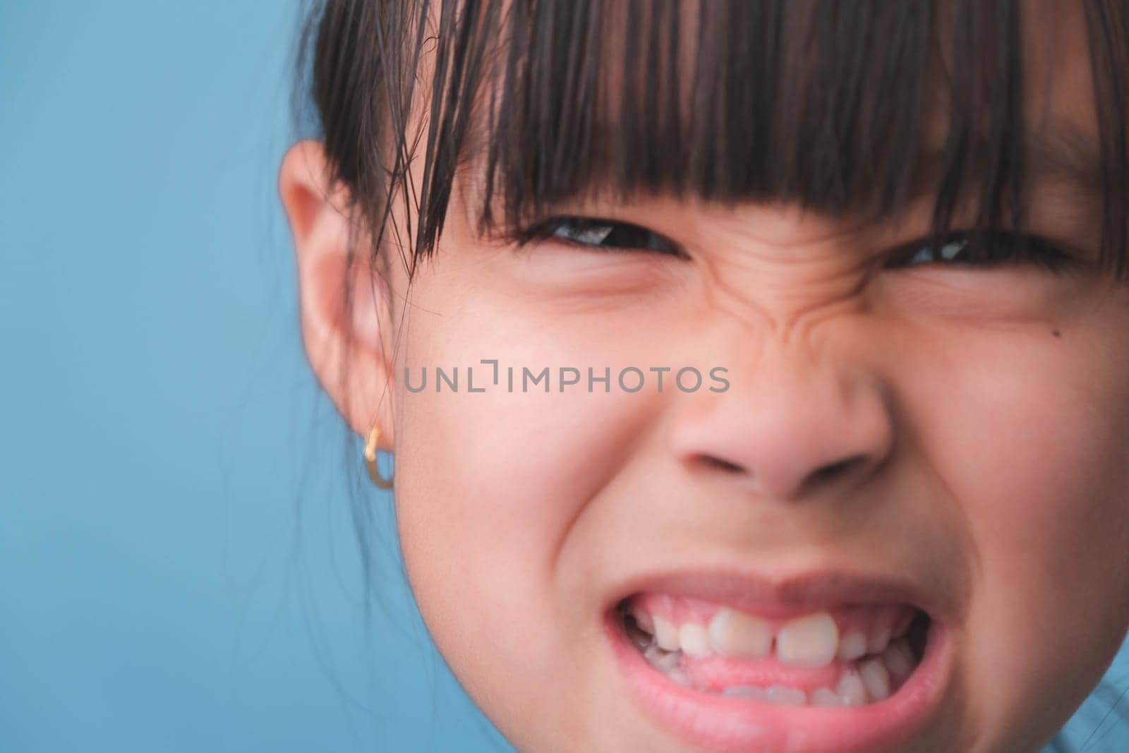 Close-up of smiling young girl revealing her beautiful white teeth on a blue background. Concept of good health in childhood. by TEERASAK