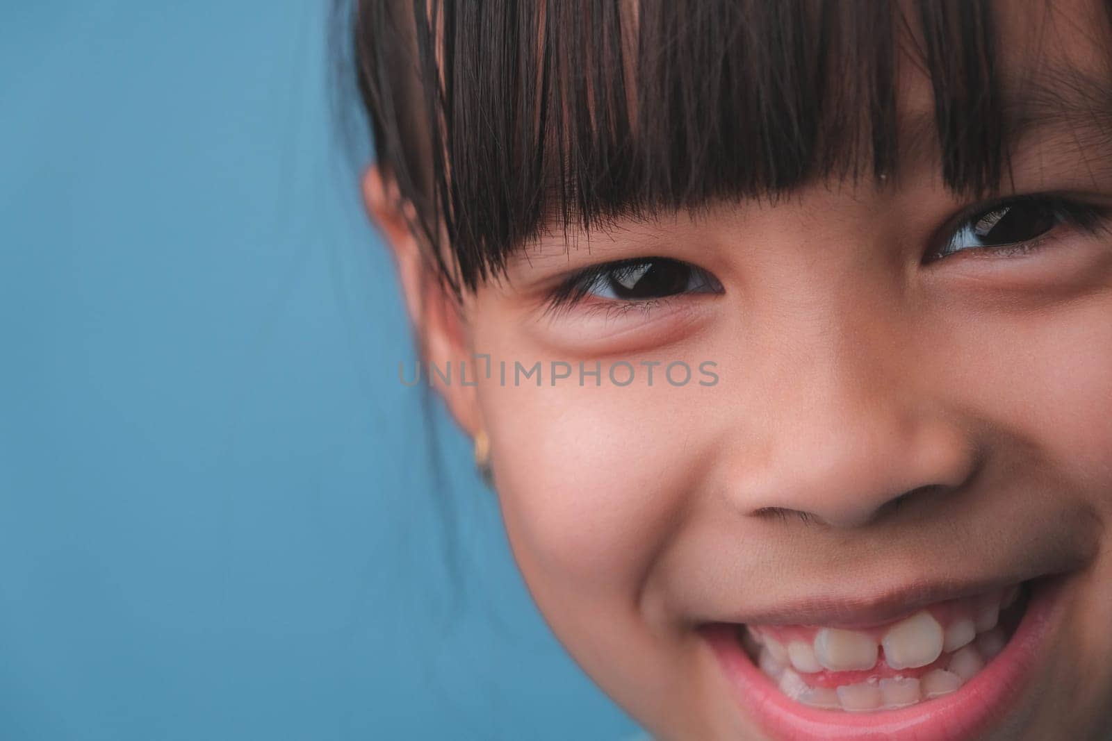 Portrait of a smiling little girl looking at the camera. Close up of cute Asian girl face posing on blue background.