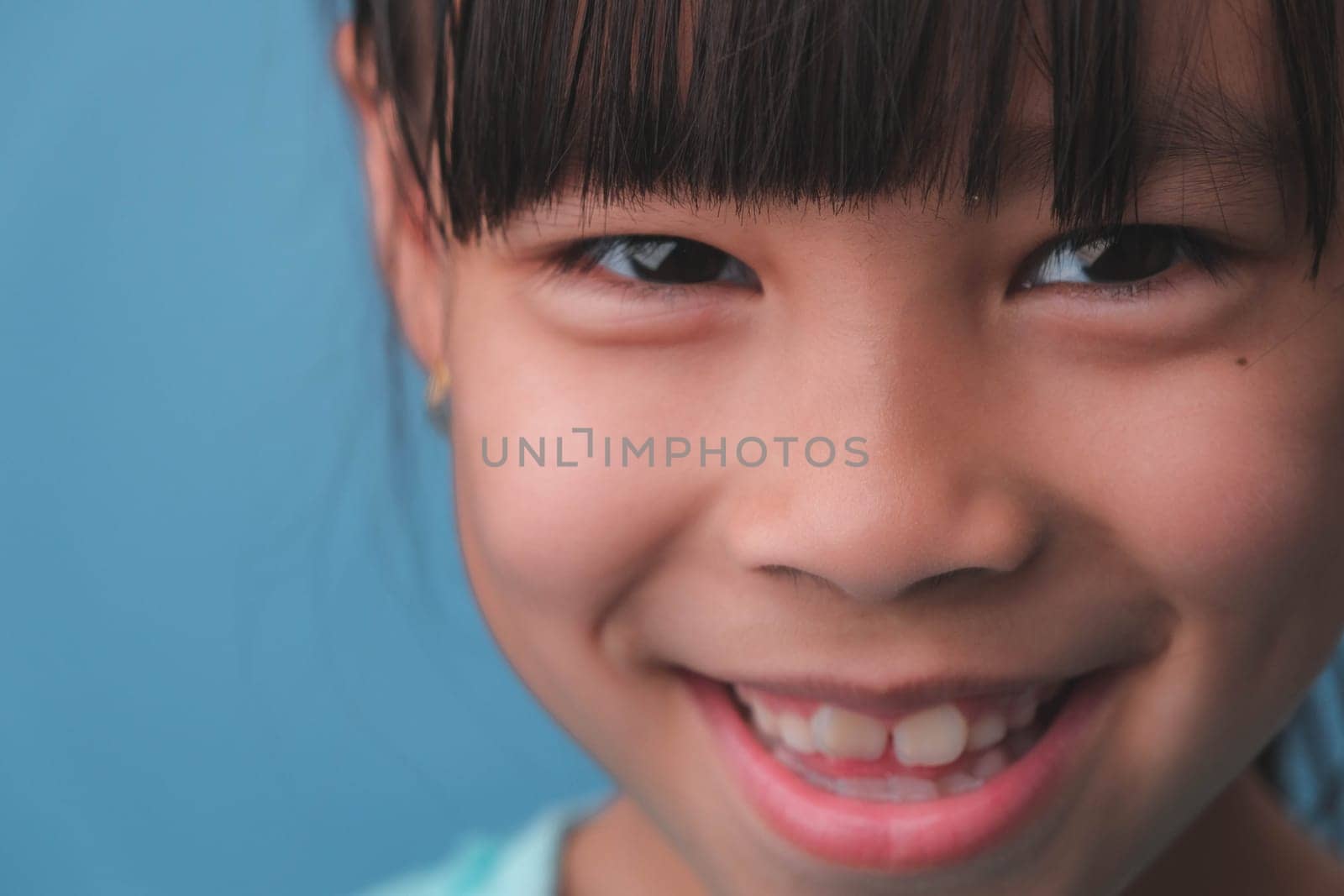 Close-up of smiling young girl revealing her beautiful white teeth on a blue background. Concept of good health in childhood. by TEERASAK