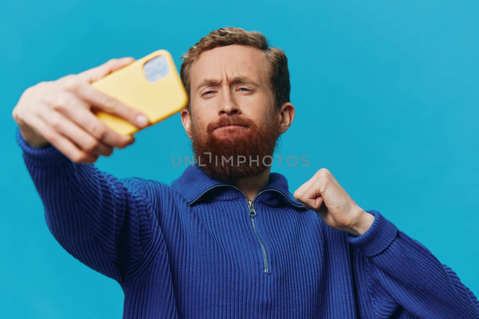 Portrait of a man with a phone in his hands blogger takes selfies, on a blue background. Communicating online social media, lifestyle by SHOTPRIME