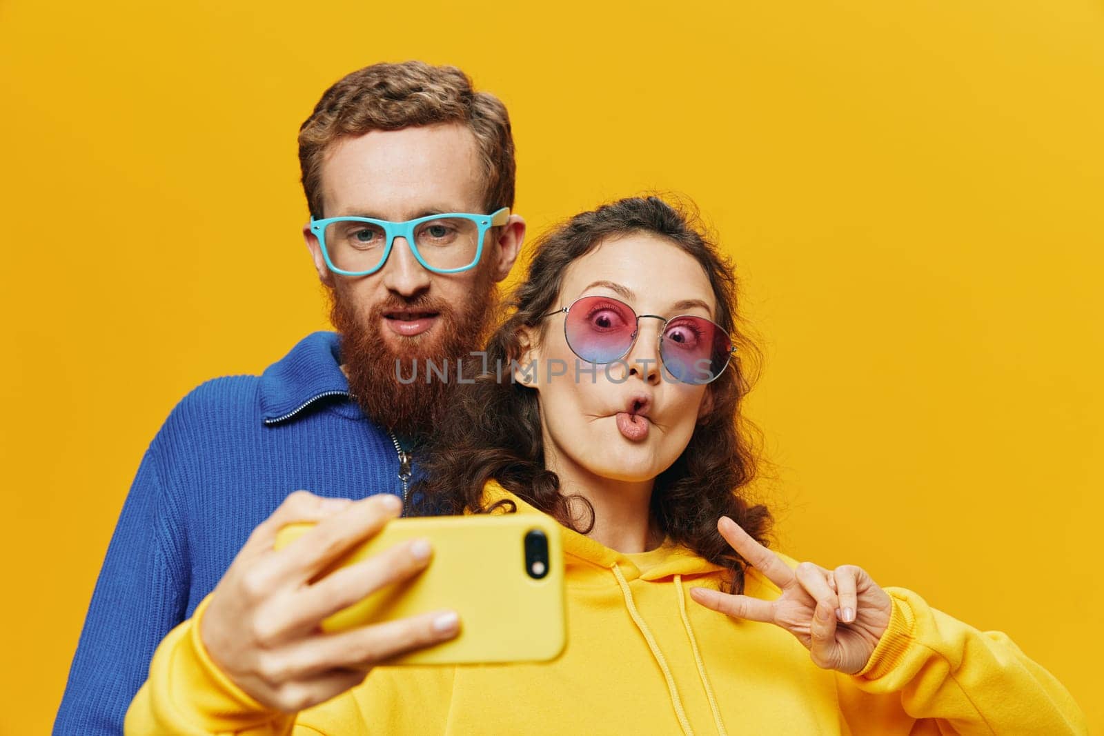 Woman and man funny couple with phones in hand social networking and communication crooked do selfies smile fun, on yellow background. The concept of real family relationships, freelancers, work online. High quality photo