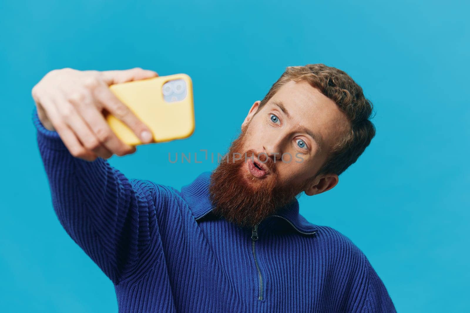 Portrait of a man with a phone in his hands blogger takes selfies, on a blue background. Communicating online social media, lifestyle by SHOTPRIME