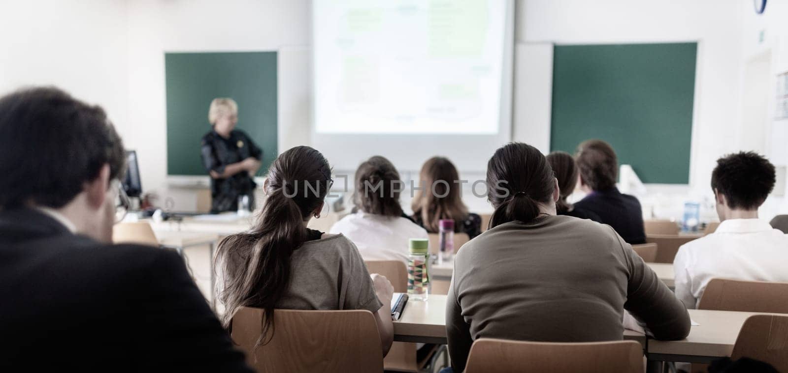 Teacher at university in front of a whiteboard screen. Students listening to lecture and making notes.