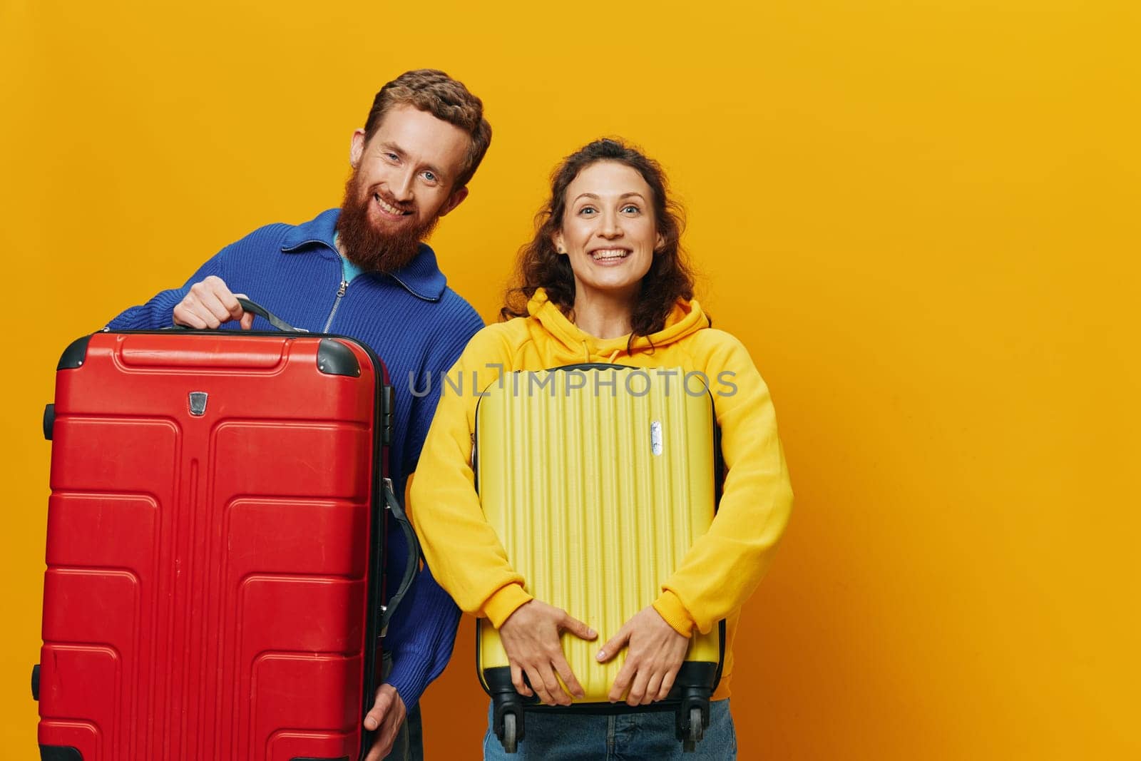 Woman and man smiling, suitcases in hand with yellow and red suitcase smiling merrily and crooked, yellow background, going on a trip, family vacation trip, newlyweds. High quality photo