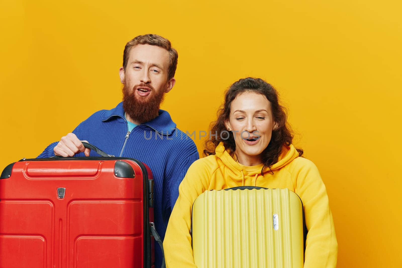 Woman and man smiling, suitcases in hand with yellow and red suitcase smiling merrily and crooked, yellow background, going on a trip, family vacation trip, newlyweds. by SHOTPRIME