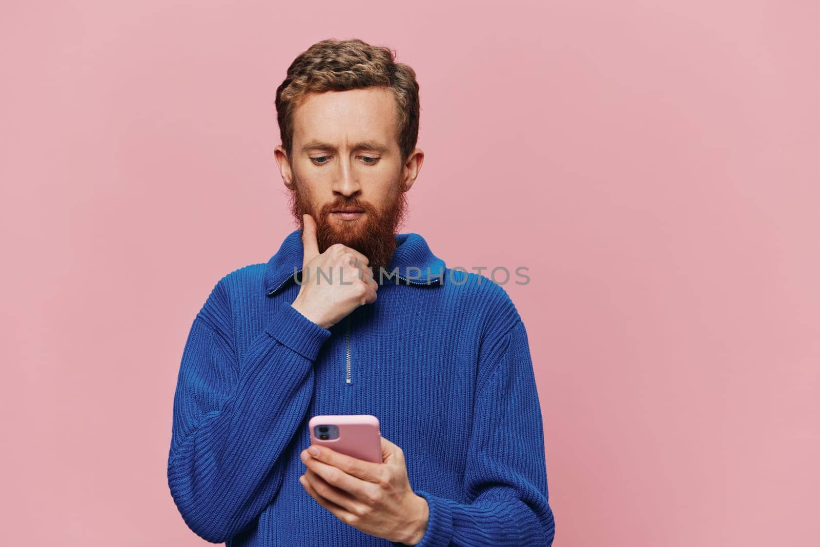 Portrait of a man with a phone in his hands doing looking at it and talking on the phone, on a pink background. Communicating online social media, lifestyle. High quality photo