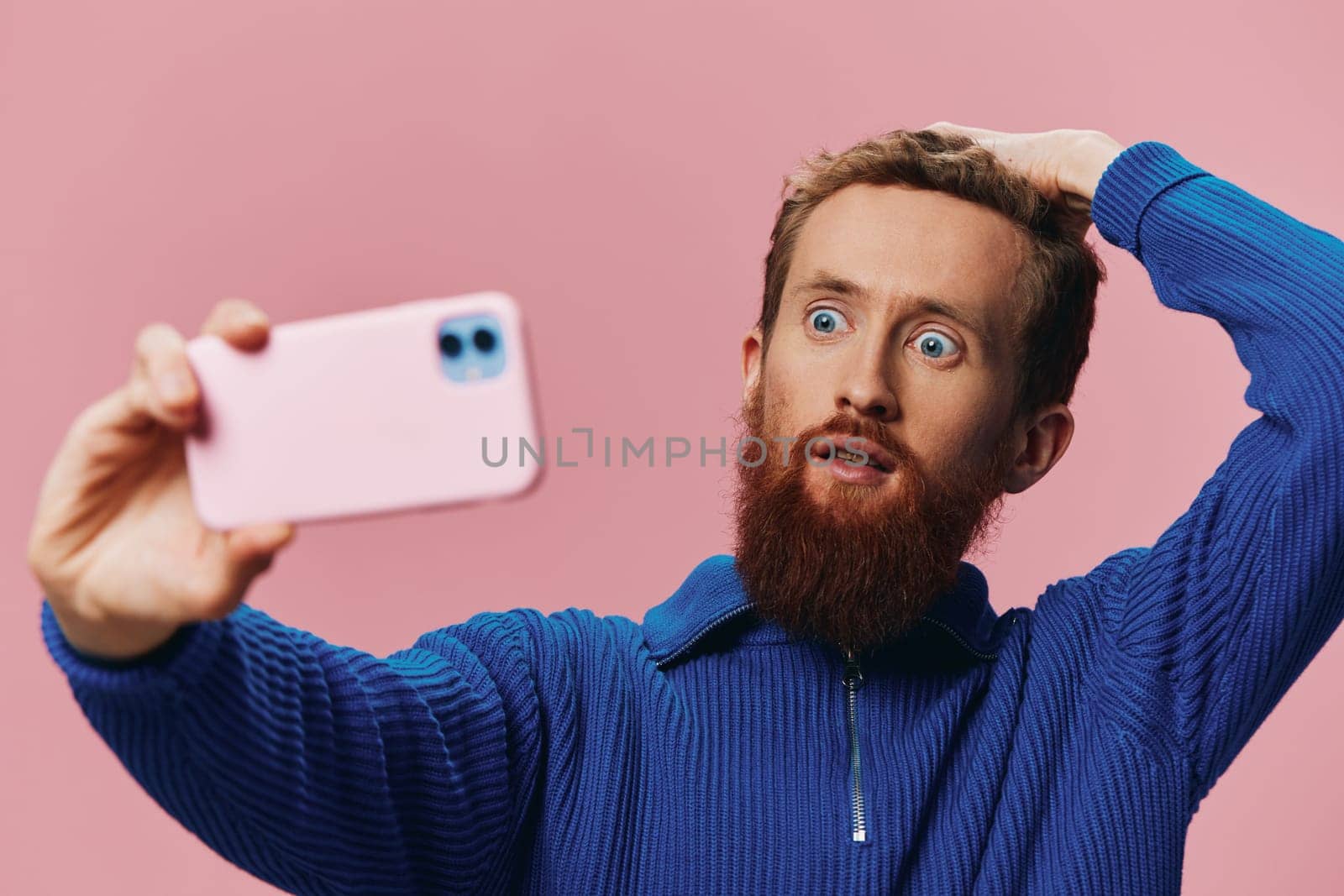 Portrait of a redheaded man with phone in hand taking selfies and photos on his phone with a smile on a pink background, blogger by SHOTPRIME