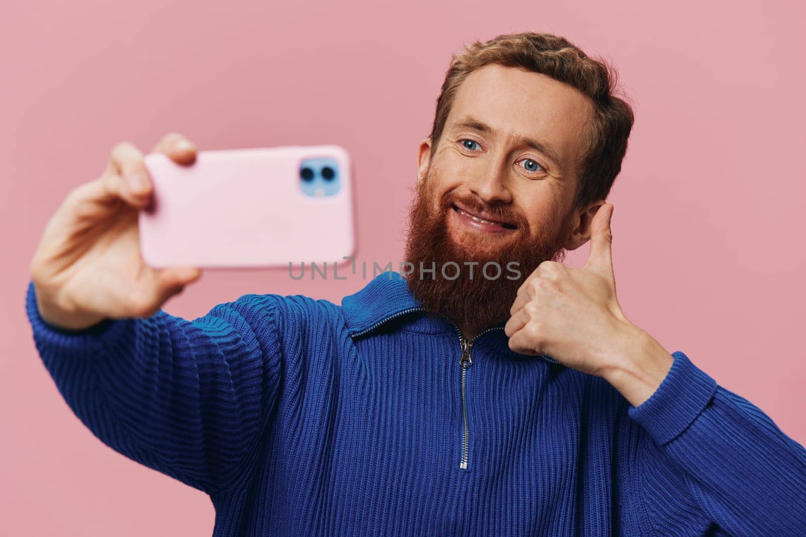 Portrait of a redheaded man with phone in hand taking selfies and photos on his phone with a smile on a pink background, blogger by SHOTPRIME