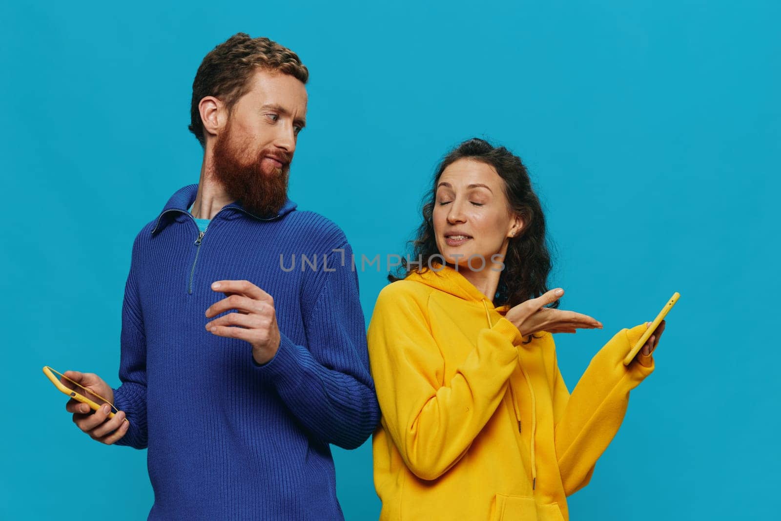 Woman and man cheerful couple with phones in their hands crooked smile cheerful, on blue background. The concept of real family relationships, talking on the phone, work online. High quality photo