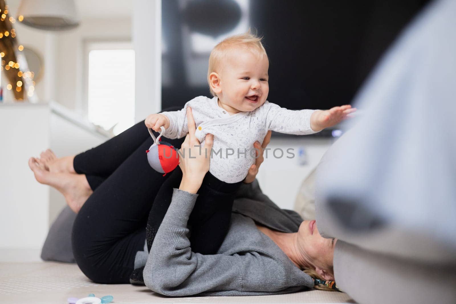 Happy family moments. Mother lying comfortably on children's mat playing with her baby boy watching and suppervising his first steps. Positive human emotions, feelings, joy