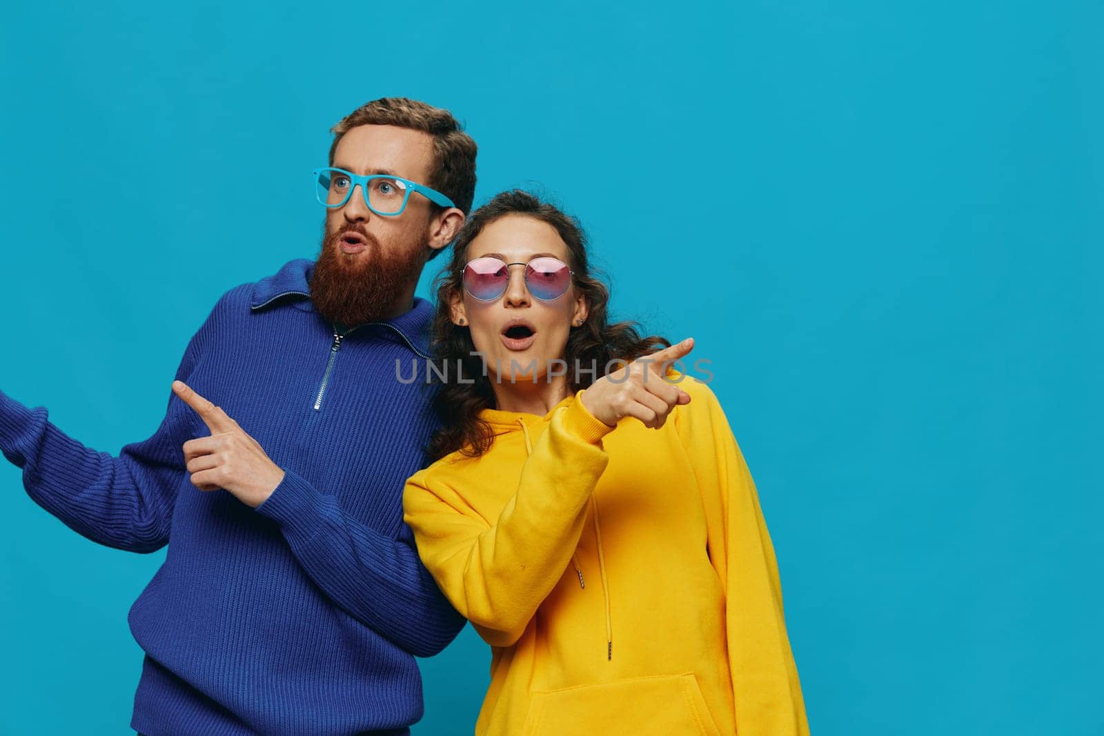 A woman and a man fun couple cranking and showing signs with their hands smiling cheerfully, on a blue background, The concept of a real relationship in a family. by SHOTPRIME