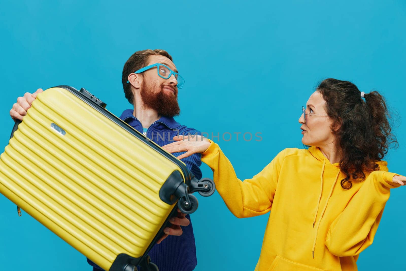 Woman and man smile sitting on suitcase with yellow suitcase smile, on blue background, packing for trip, family vacation trip. by SHOTPRIME