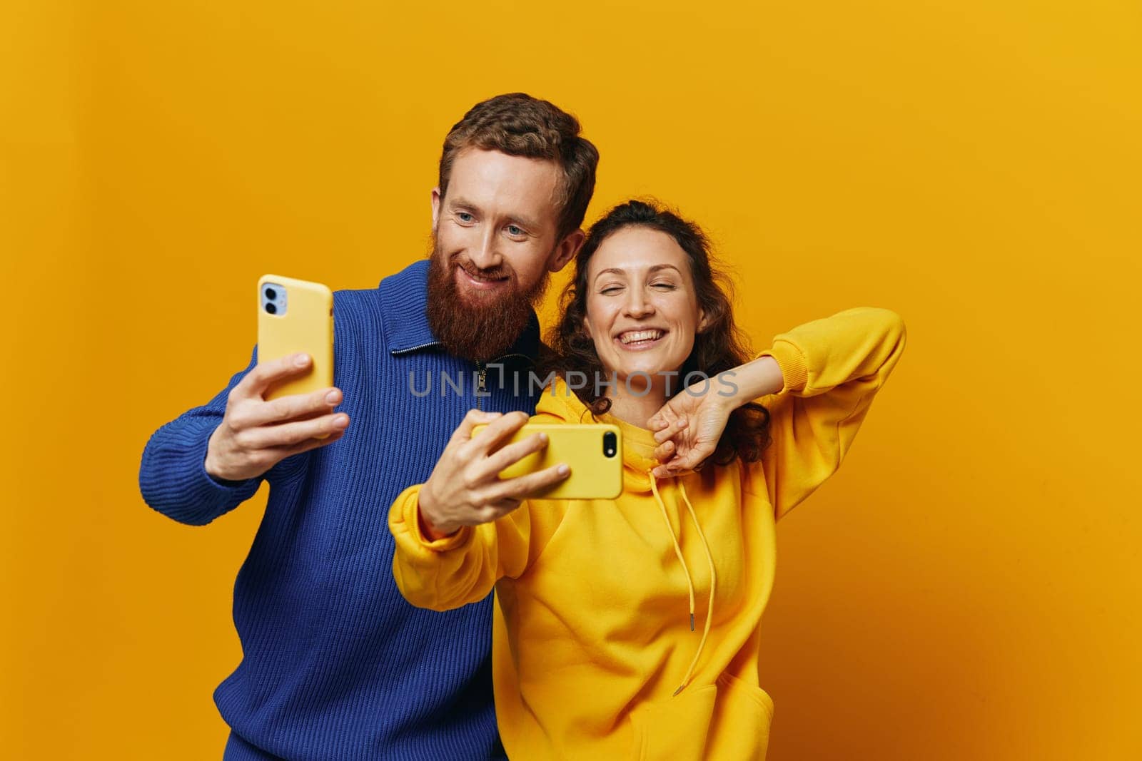 Man and woman couple smiling merrily with phone in hand social media viewing photos and videos, on yellow background, symbols signs and hand gestures, family freelancers. High quality photo