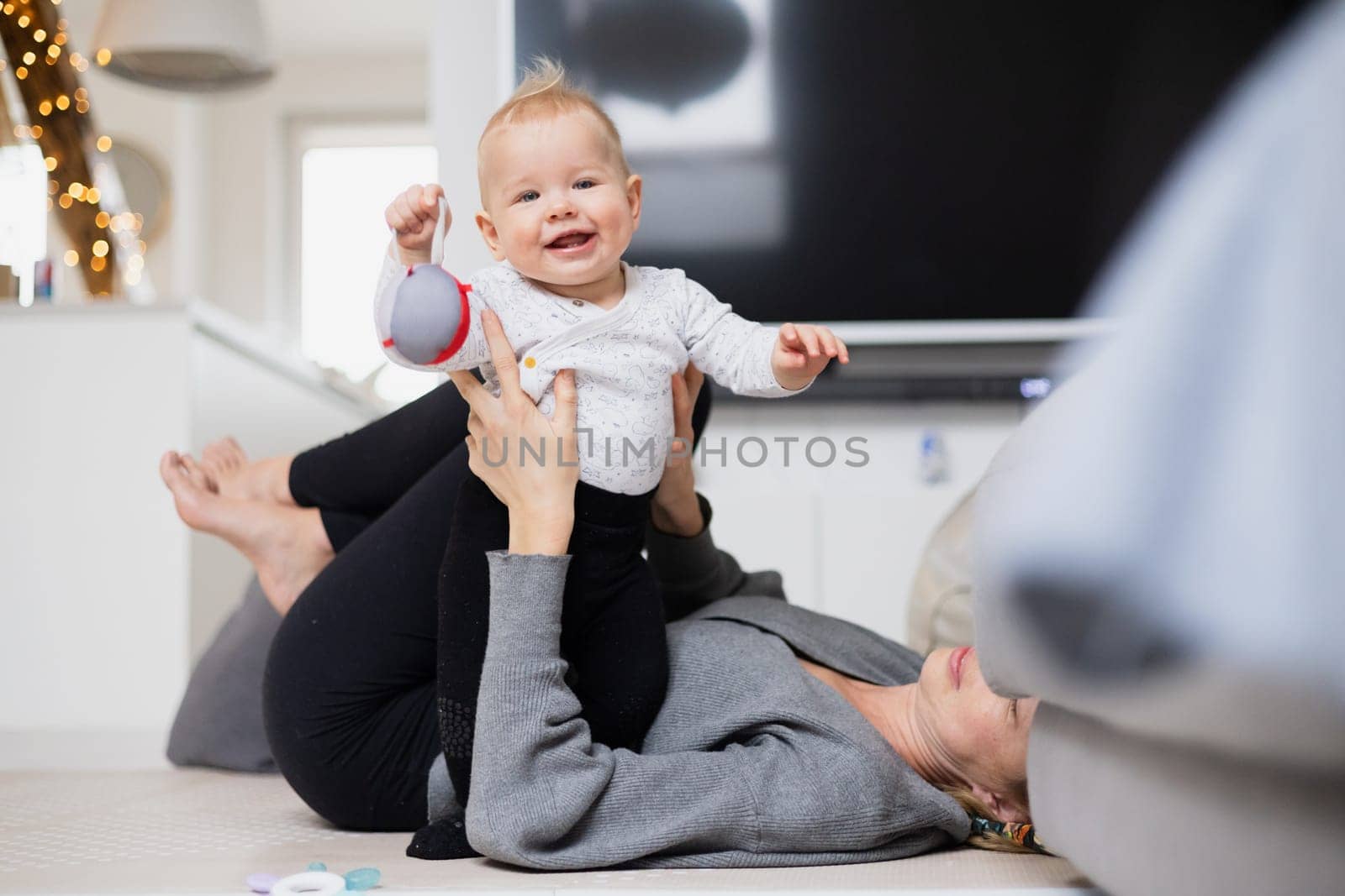 Happy family moments. Mother lying comfortably on children's mat playing with her baby boy watching and suppervising his first steps. Positive human emotions, feelings, joy. by kasto