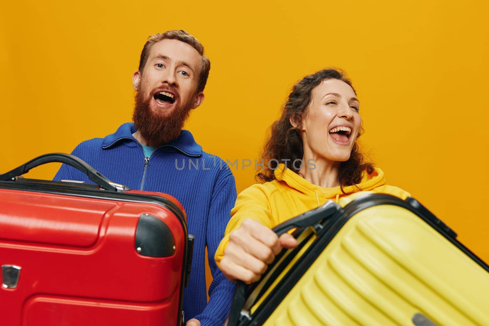 Woman and man smiling, suitcases in hand with yellow and red suitcase smiling merrily and crooked, yellow background, going on a trip, family vacation trip, newlyweds. High quality photo