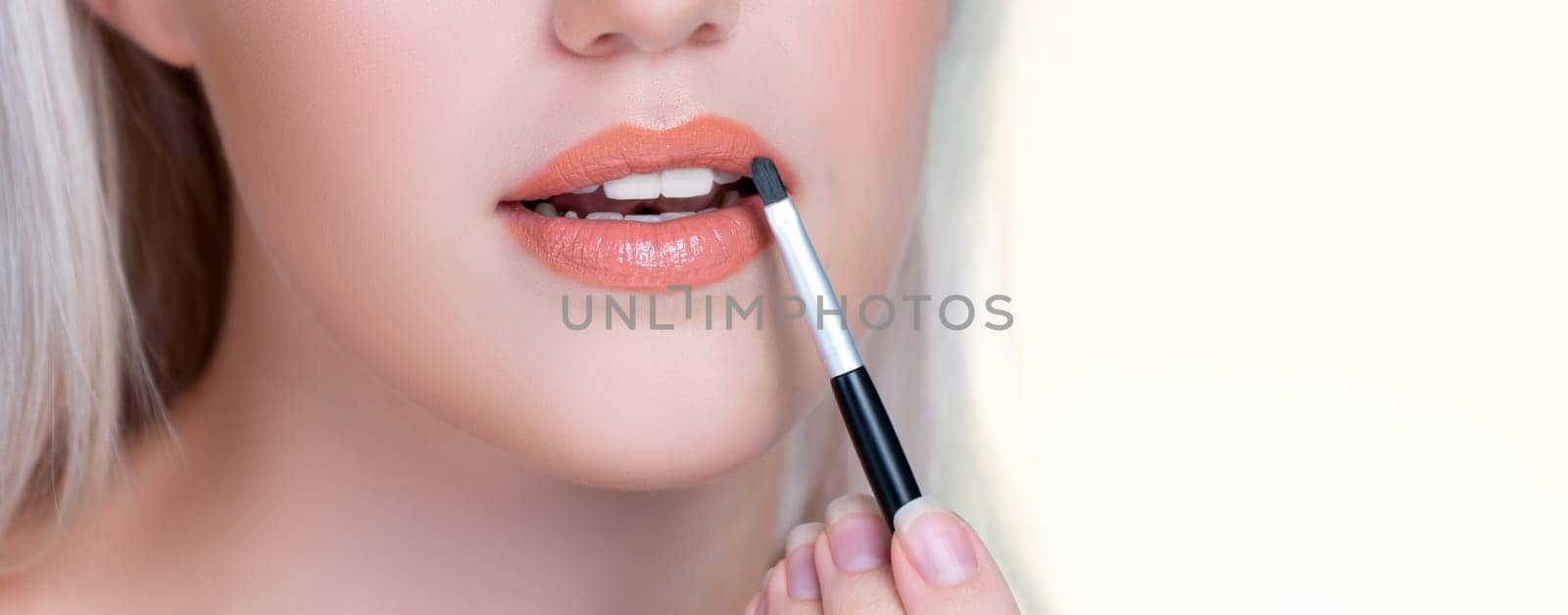 Closeup personable young woman putting alluring fashion glossy lipstick. by biancoblue