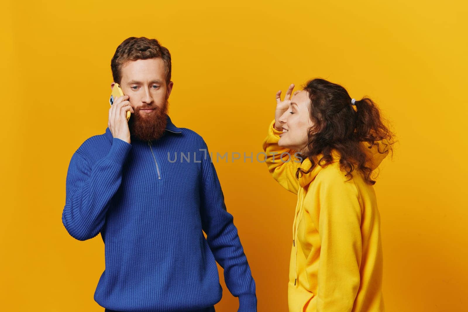 Man and woman couple with phone in hand call talking on the phone, on a yellow background, symbols signs and hand gestures, family quarrel jealousy and scandal. High quality photo