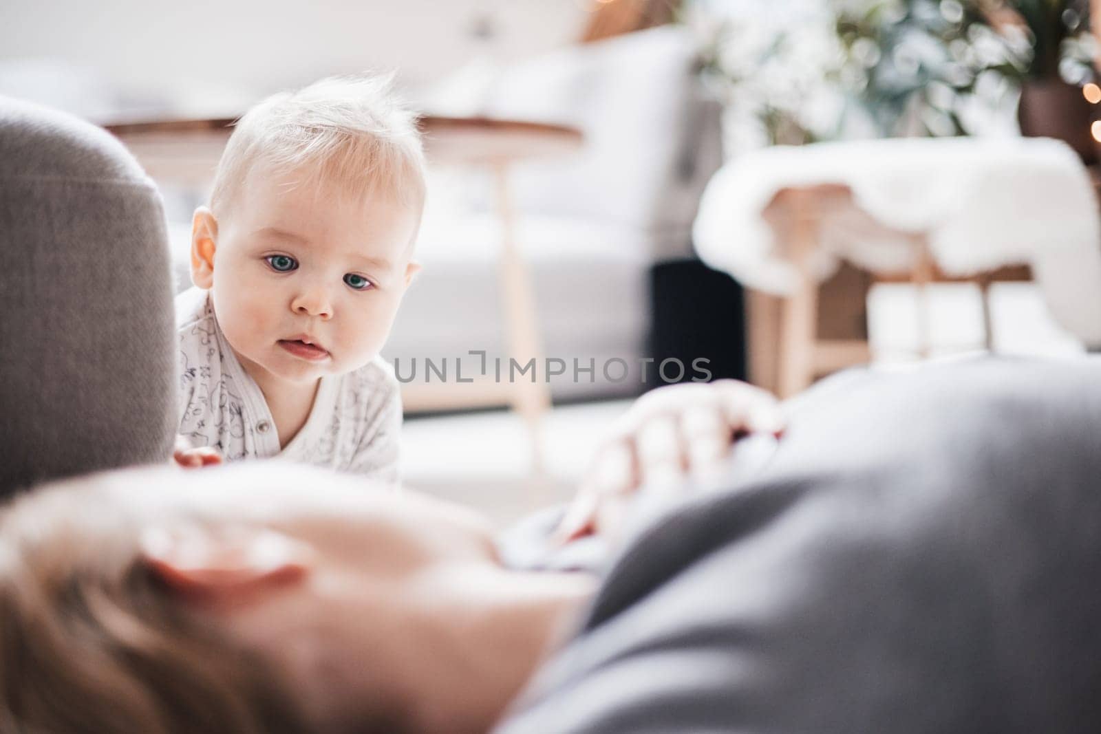 Happy family moments. Mother lying comfortably on children's mat playing with her baby boy watching and suppervising his first steps. Positive human emotions, feelings, joy. by kasto