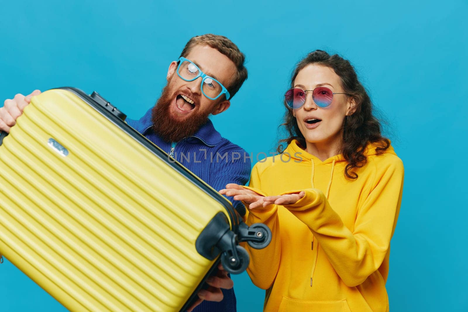 Woman and man smile sitting on suitcase with yellow suitcase smile, on blue background, packing for trip, family vacation trip. High quality photo