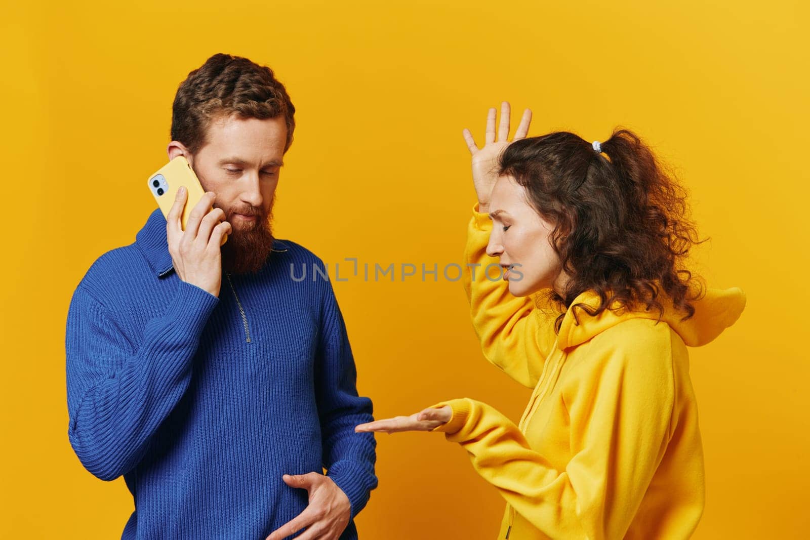 Man and woman couple with phone in hand call talking on the phone, on a yellow background, symbols signs and hand gestures, family quarrel jealousy and scandal. High quality photo