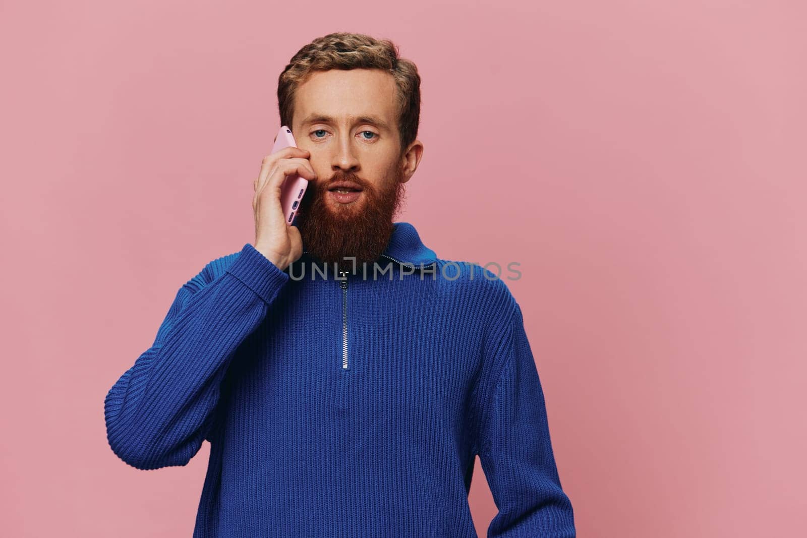 Portrait of a man with a phone in his hands doing looking at it and talking on the phone, on a pink background. Communicating online social media, lifestyle. High quality photo