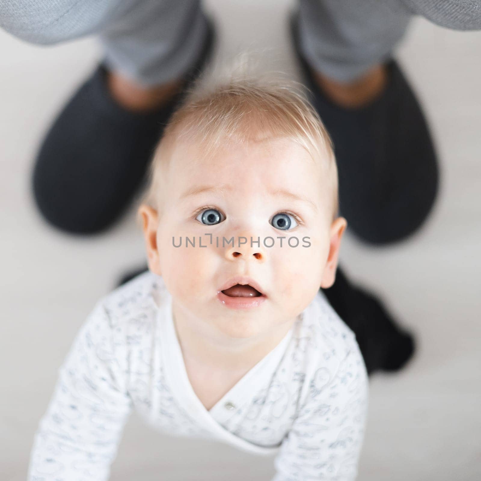 Top down view of cheerful baby boy infant taking first steps holding to father's sweatpants at home. Cute baby boy learning to walk.