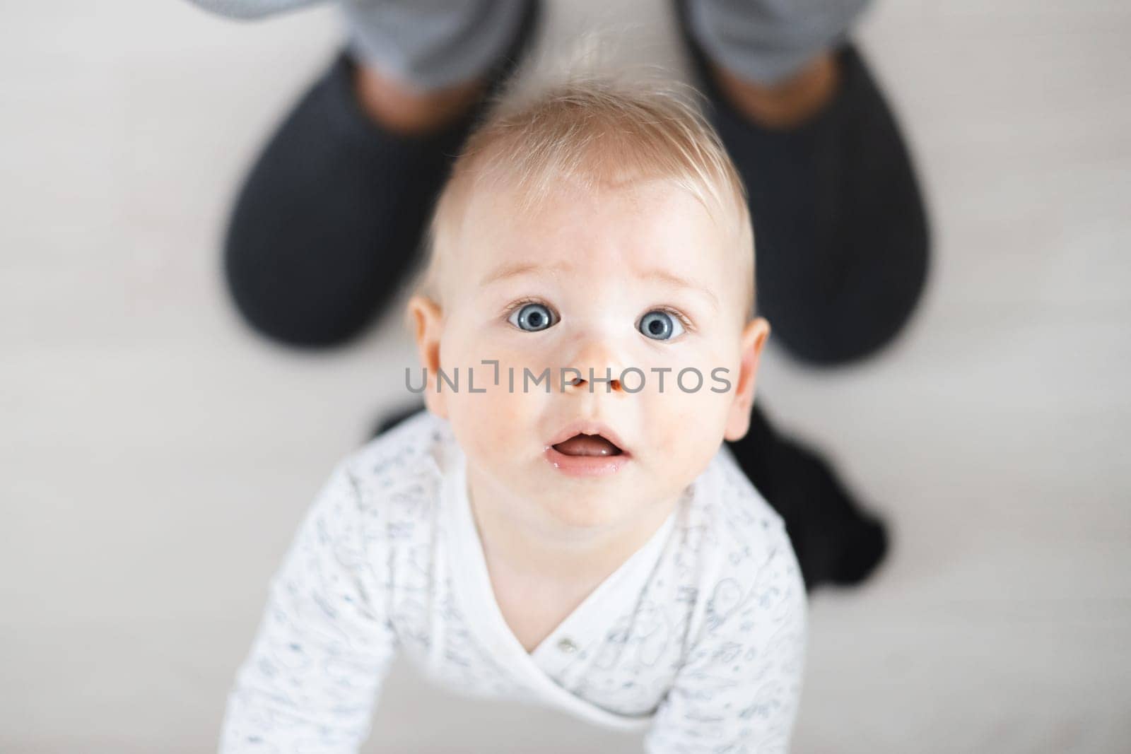 Top down view of cheerful baby boy infant taking first steps holding to father's sweatpants at home. Cute baby boy learning to walk.