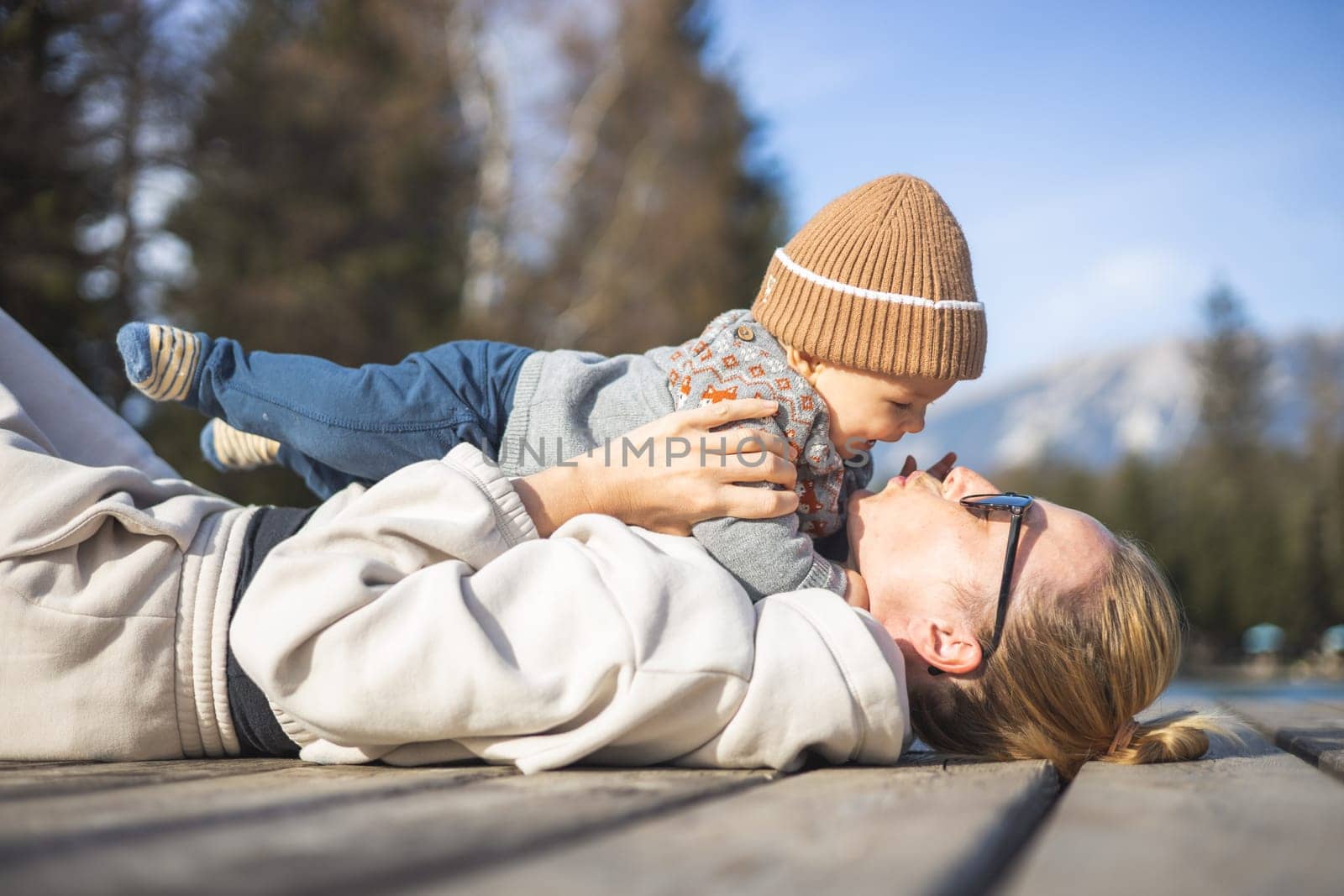 Happy family. Young mother playing with her baby boy infant oudoors on sunny autumn day. Portrait of mom and little son on wooden platform by lake. Positive human emotions, feelings, joy