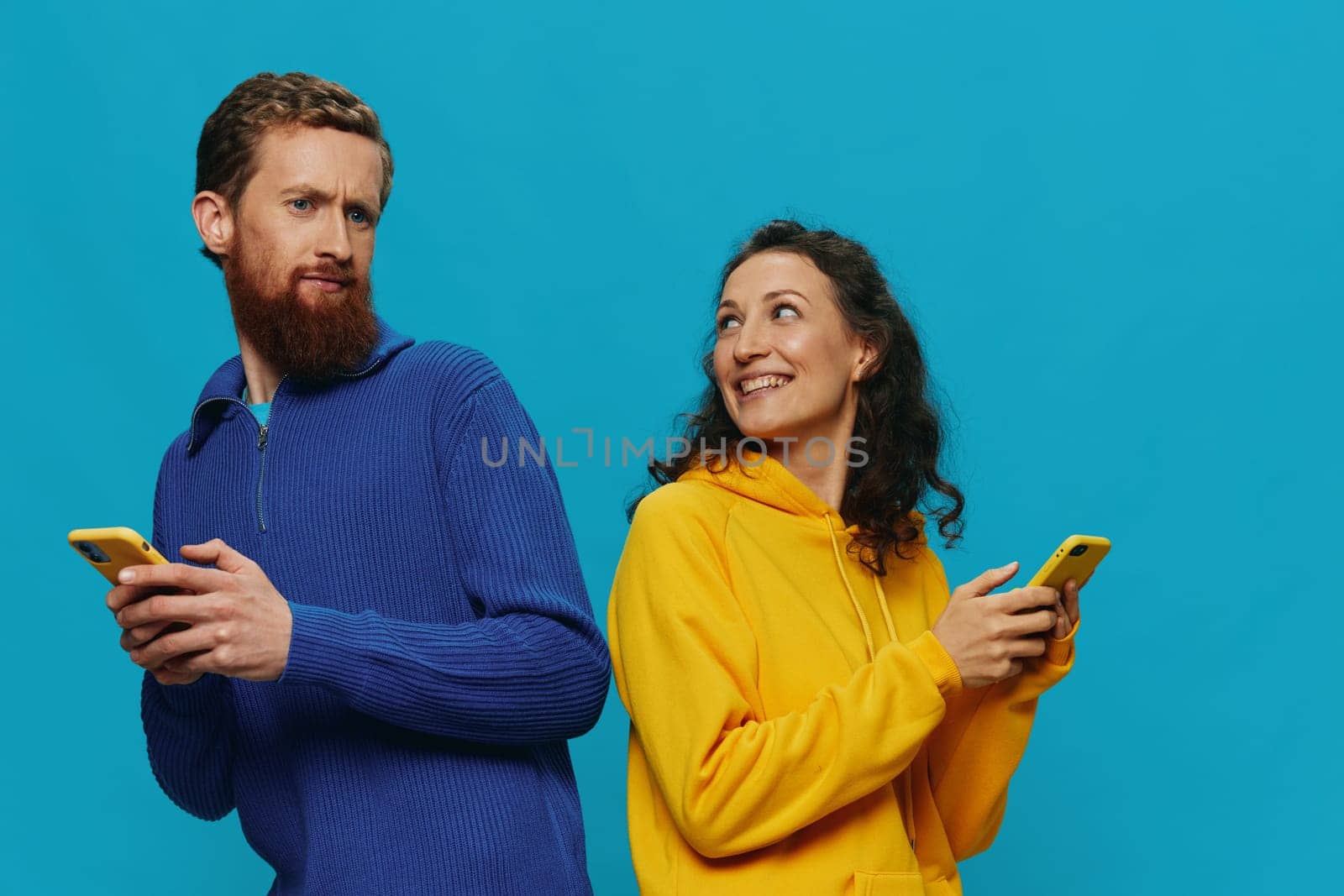 Woman and man cheerful couple with phones in their hands crooked smile cheerful, on blue background. The concept of real family relationships, talking on the phone, work online. High quality photo