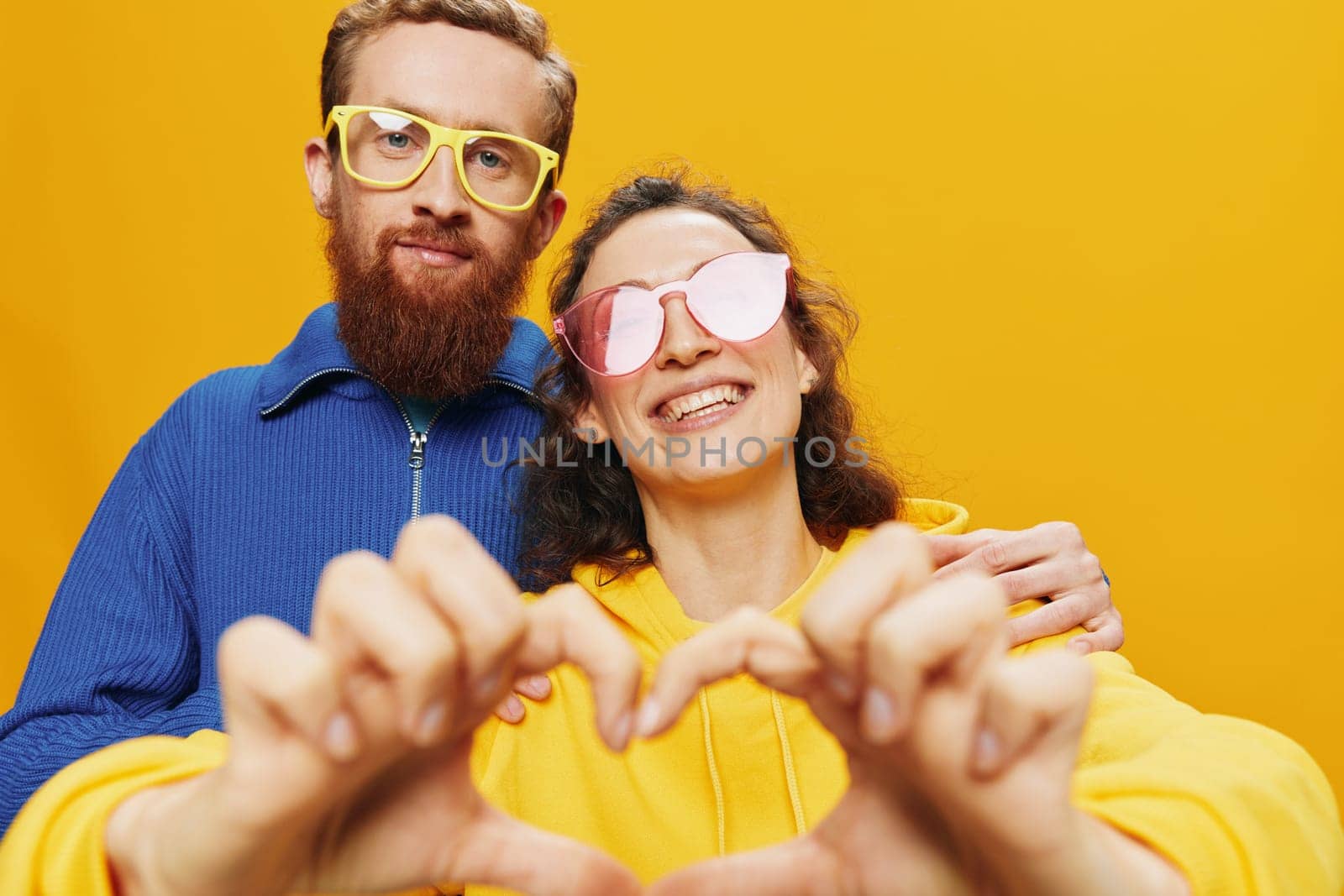 Man and woman couple smiling cheerfully and crooked with glasses, on yellow background, symbols signs and hand gestures, family shoot, newlyweds. High quality photo