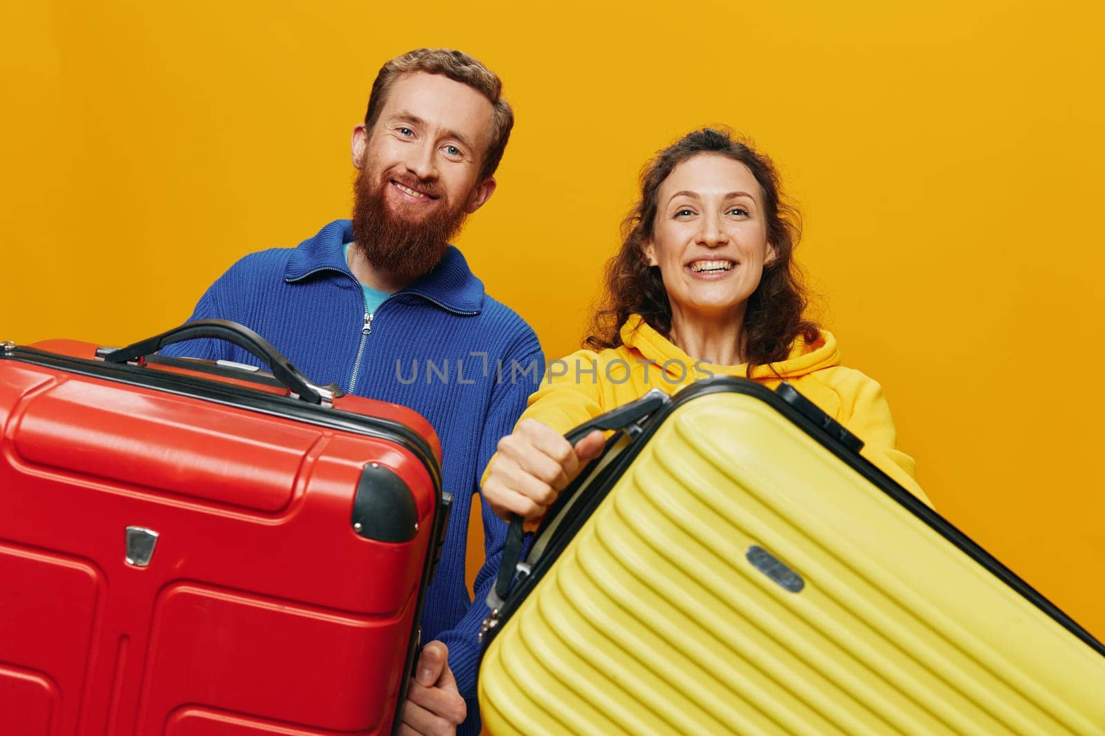 Woman and man smiling, suitcases in hand with yellow and red suitcase smiling merrily and crooked, yellow background, going on a trip, family vacation trip, newlyweds. by SHOTPRIME