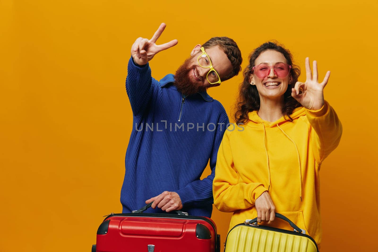 Woman and man smiling, suitcases in hand with yellow and red suitcase smiling merrily and crooked, yellow background, going on a trip, family vacation trip, newlyweds. High quality photo