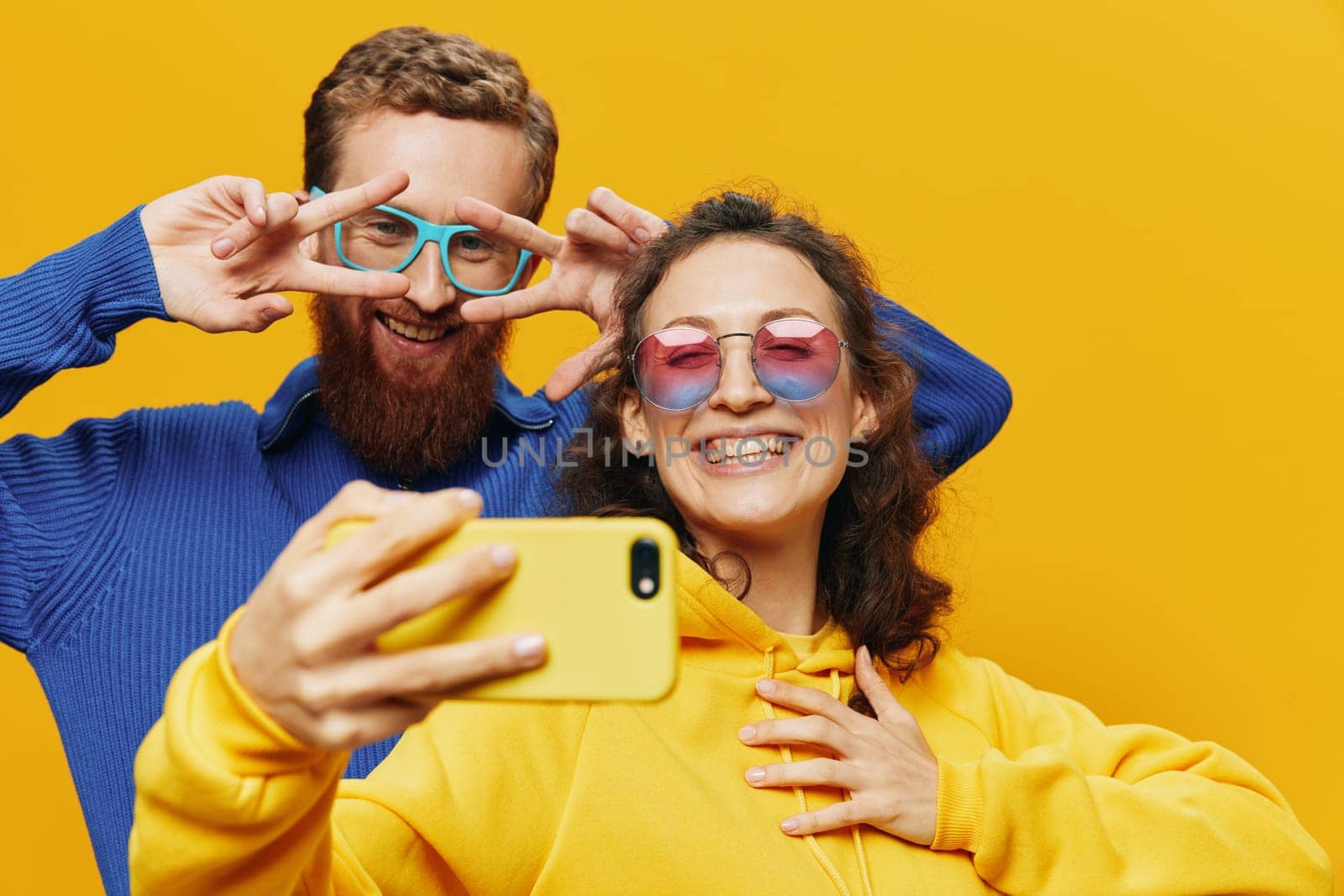 Woman and man funny couple with phones in hand social networking and communication crooked do selfies smile fun, on yellow background. The concept of real family relationships, freelancers, work online. High quality photo