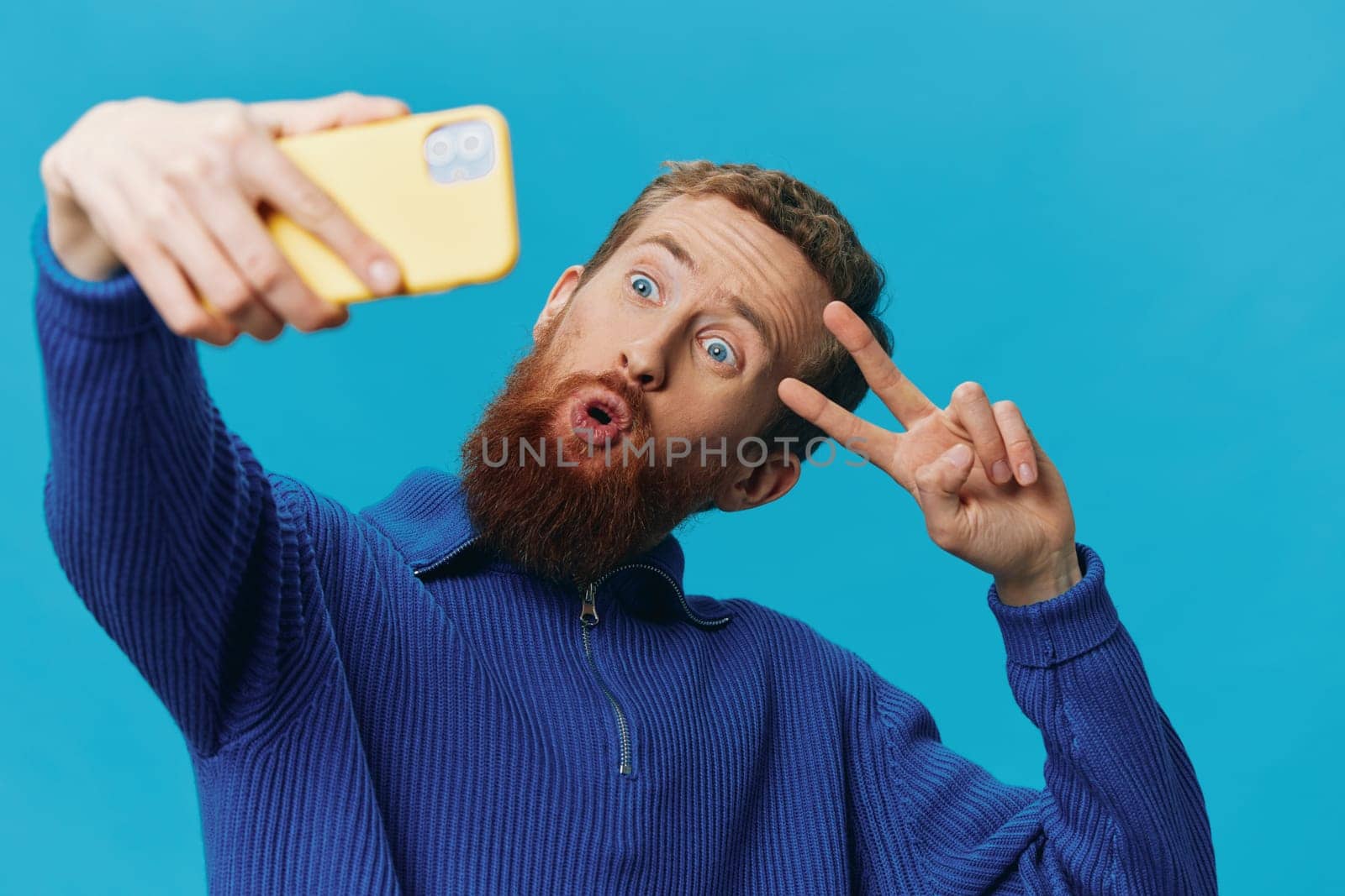 Portrait of a man with a phone in his hands blogger takes selfies, on a blue background. Communicating online social media, lifestyle. High quality photo