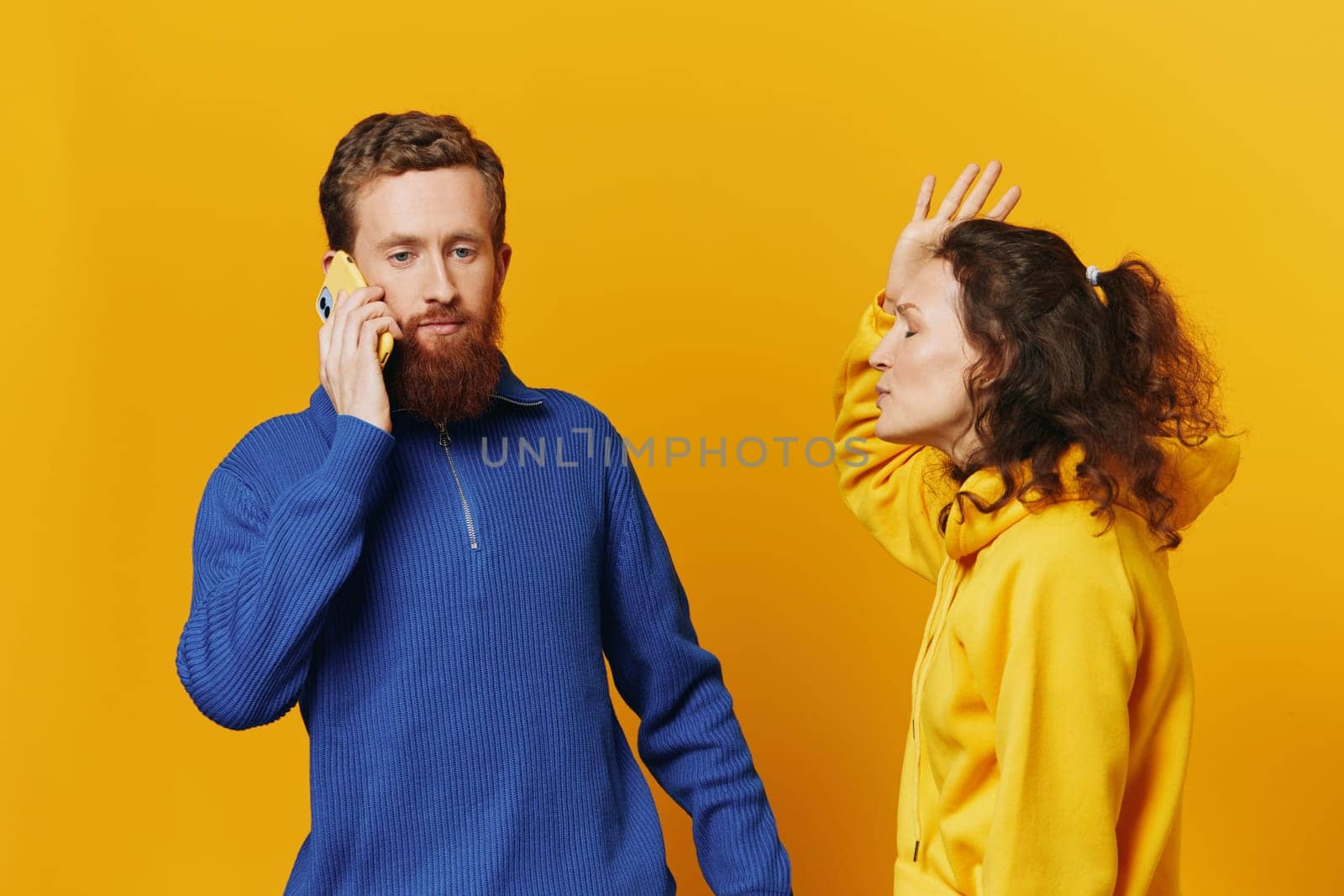 Man and woman couple with phone in hand call talking on the phone, on a yellow background, symbols signs and hand gestures, family quarrel jealousy and scandal. by SHOTPRIME