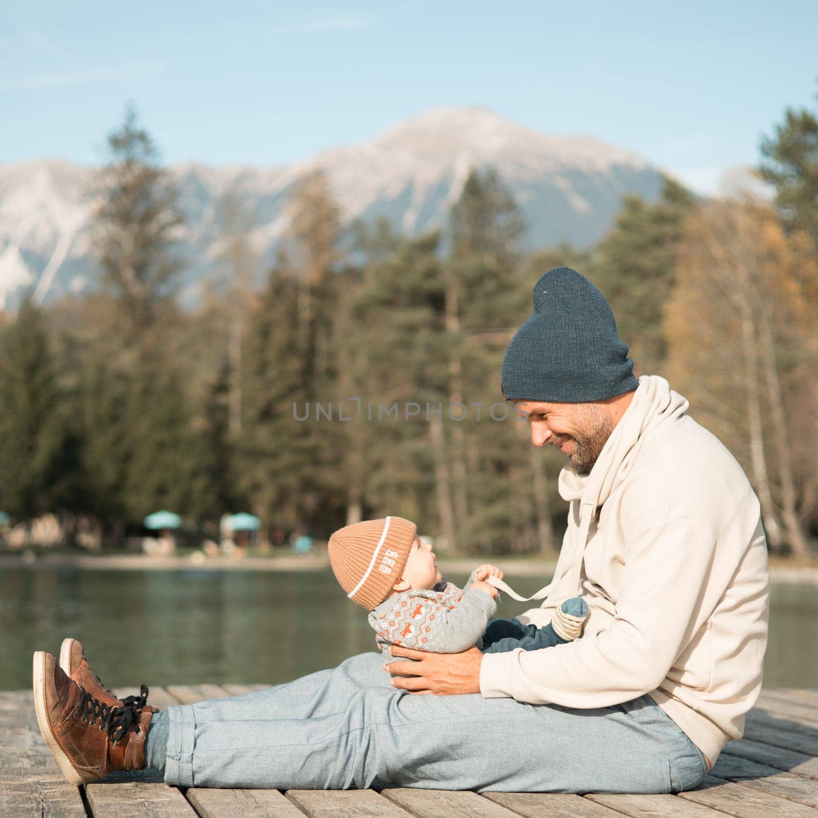 Happy family. Father playing with her baby boy infant oudoors on sunny autumn day. Portrait of dad and little son on wooden platform by lake. Positive human emotions, feelings, joy. by kasto